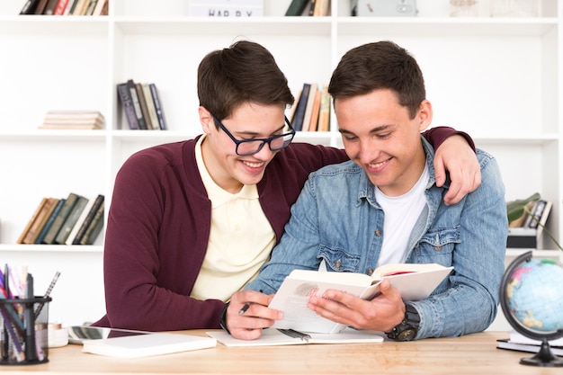 Kostenloses Foto jungenklassenkameraden, die bei tisch sitzen und buch in der klasse lesen