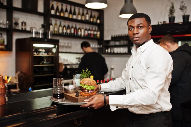 Junger afrikanisch-amerikanischer Kellner hält Tablett mit Burger an der Bar des Restaurants