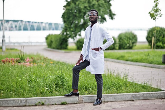 Junger afrikanisch-amerikanischer männlicher Arzt im weißen Kittel mit einem Stethoskop posierte im Freien