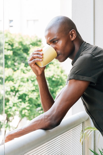 Junger afrikanischer Mann, der auf dem Geländer den Kaffee trinkend sich lehnt