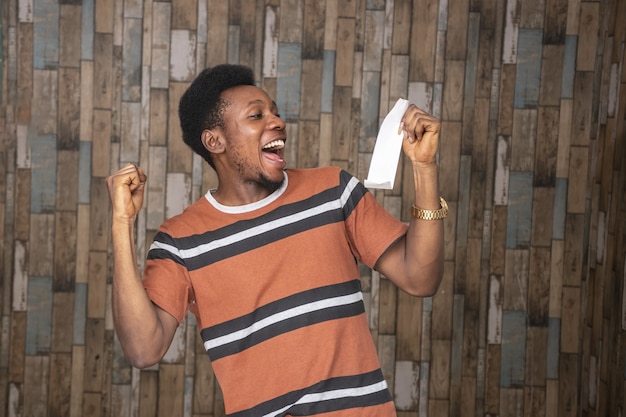 Junger afrikanischer Mann, der aufgeregt und glücklich fühlt, während er einen Zettel hält