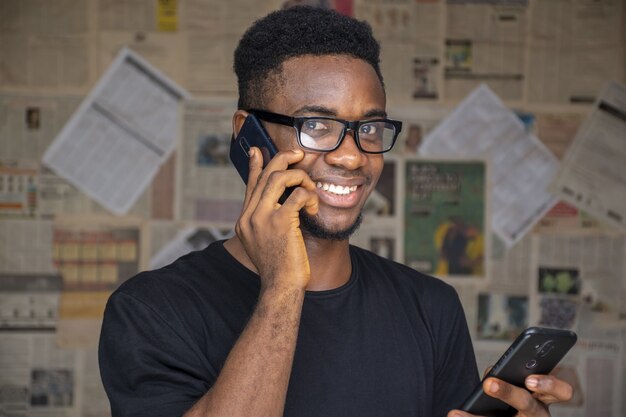 Junger afrikanischer Mann mit Brille, der am Telefon spricht, während er einen anderen in einem Raum benutzt