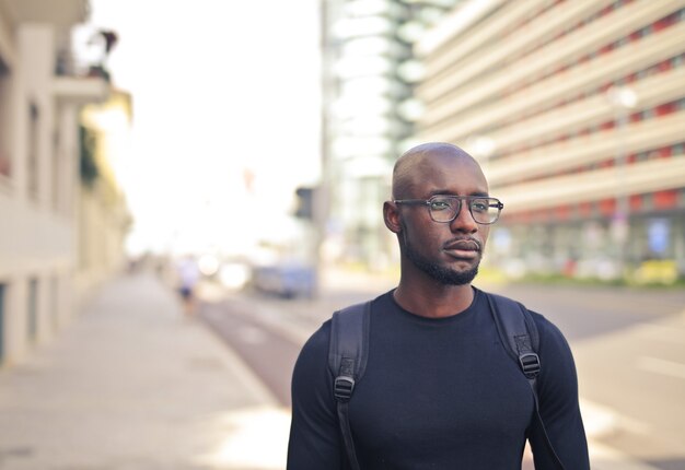 Junger afrikanischer Mann mit Brille, die ein schwarzes T-Shirt und einen Rucksack in der Straße trägt