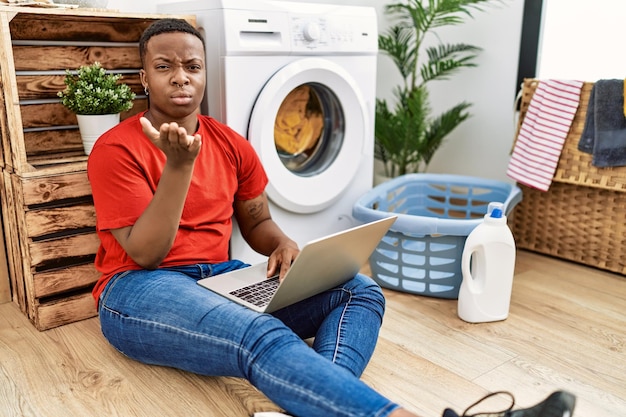 Kostenloses Foto junger afrikanischer mann wäscht wäsche und benutzt den computer, schaut in die kamera und wirft einen kuss mit der hand in die luft, was ein schöner und sexy liebesausdruck ist