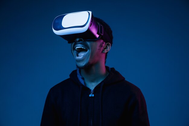 Junger Afroamerikaner spielt in VR-Brille im Neonlicht auf Gradient