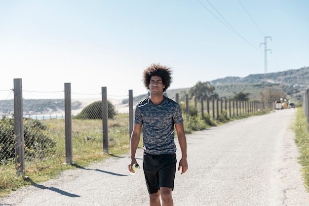 Junger Afroamerikanermann in der Sportkleidung gehend entlang Straße