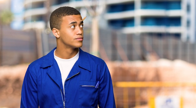 Junger afroamerikanischer arbeitskraftmann, der oben mit ernstem gesicht in einer baustelle schaut