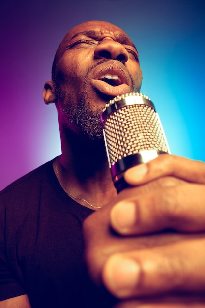 Junger afroamerikanischer Jazzmusiker, der ein Lied auf Farbverlauf lila-blau singt