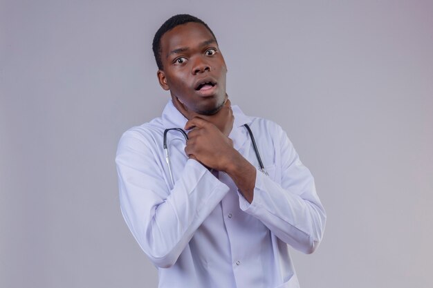 Junger afroamerikanischer männlicher Arzt, der weißen Kittel mit Stethoskop erstickt, das in Panik erstickt und seine Hände um seinen Hals hält