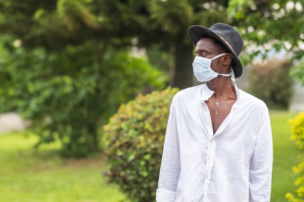 Junger afroamerikanischer Mann, der eine schützende Gesichtsmaske trägt und im Freien posiert