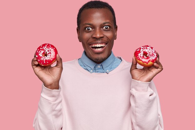 Junger afroamerikanischer Mann, der leckere Donuts hält