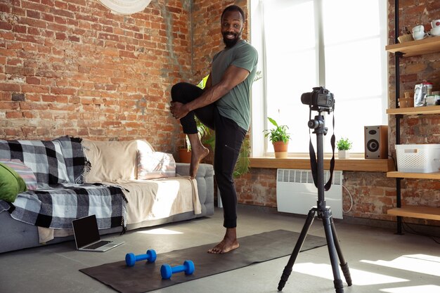 Junger afroamerikanischer Mann, der zu Hause Online-Fitnesskurse unterrichtet