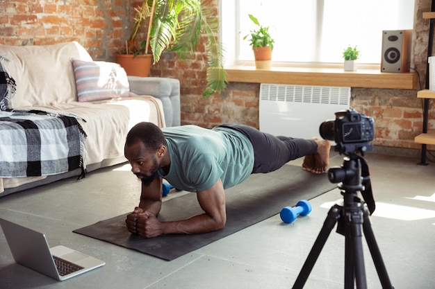 Junger afroamerikanischer Mann, der zu Hause Online-Fitnesskurse unterrichtet