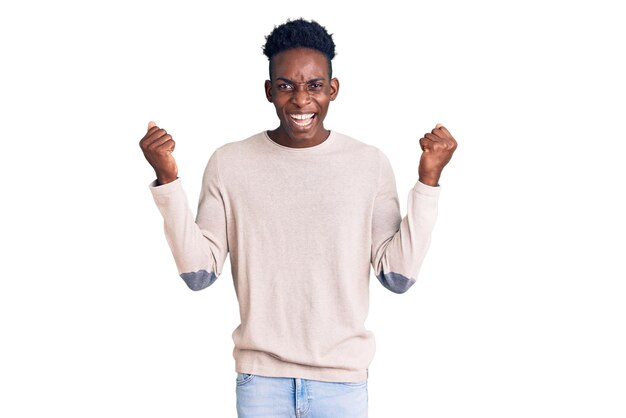 Junger afroamerikanischer Mann in lässiger Kleidung schreit stolz, feiert Sieg und Erfolg sehr aufgeregt mit erhobenen Armen