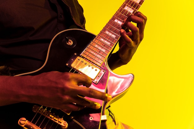 Junger afroamerikanischer Musiker, der die Gitarre wie ein Rockstar auf gelbem Hintergrund im Neonlicht spielt.