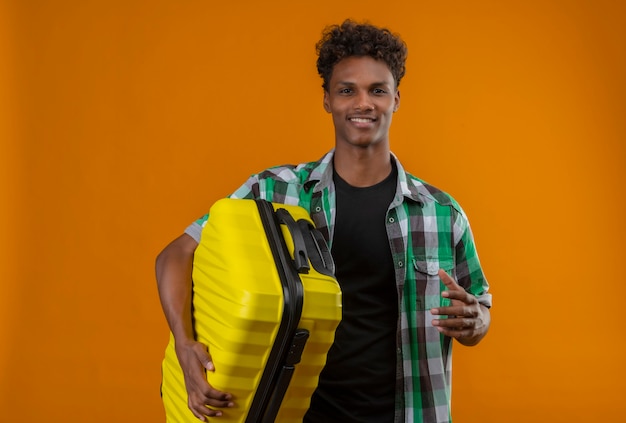 Kostenloses Foto junger afroamerikanischer reisender mann, der koffer hält, der fröhlich, positiv und glücklich lächelt