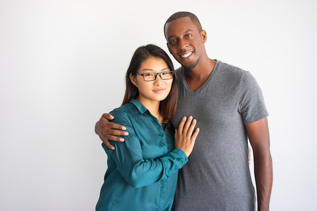 Junger afroer-amerikanisch Mann, der seine asiatische Freundin mit Gläsern umarmt.