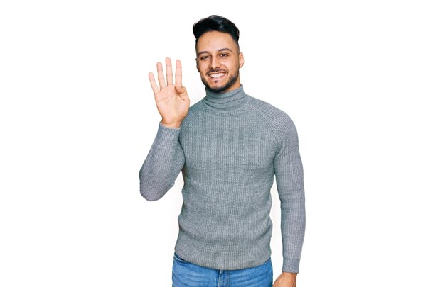 Junger arabischer Mann in lässiger Kleidung zeigt mit Finger Nummer vier nach oben und lächelt dabei selbstbewusst und glücklich