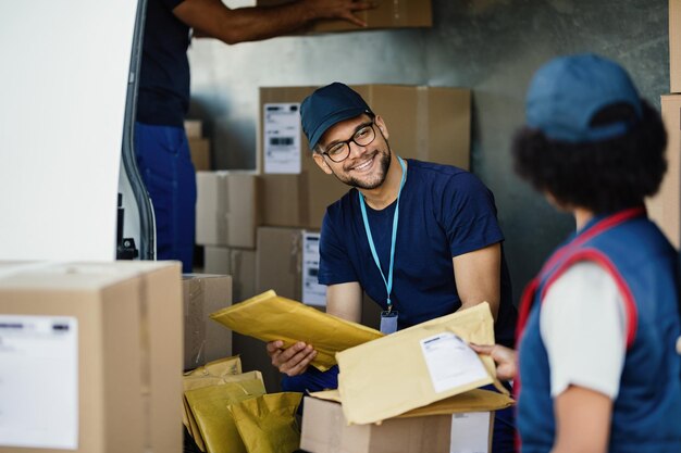 Junger Arbeiter im Gespräch mit seiner Kollegin beim Sortieren von Paketen für den Versand in einem Lieferwagen