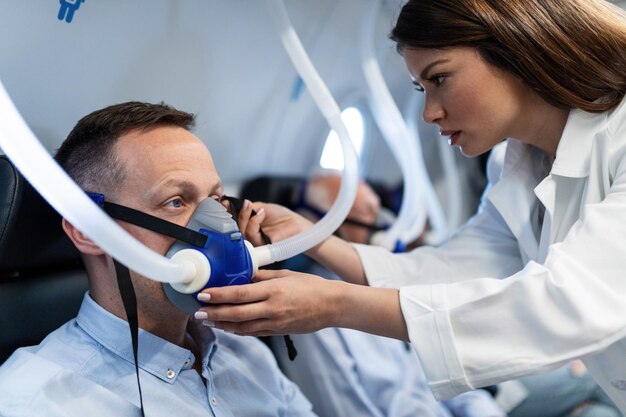 Junger Arzt, der den Patienten während der hyperbaren Sauerstofftherapie in der Klinik mit einer Maske unterstützt