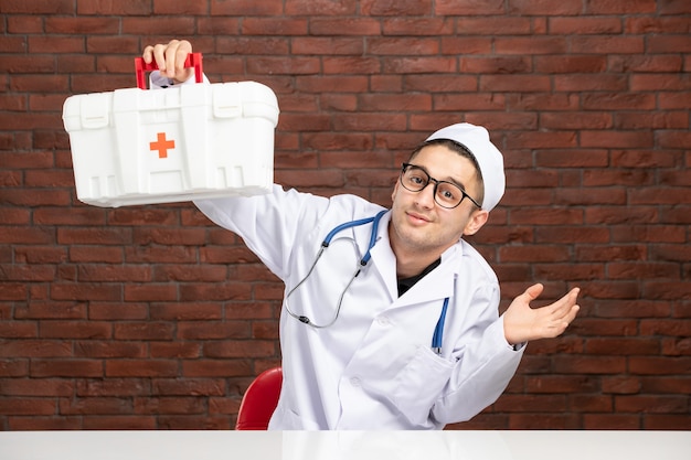 Junger Arzt der Vorderansicht im weißen medizinischen Anzug mit Erste-Hilfe-Kit