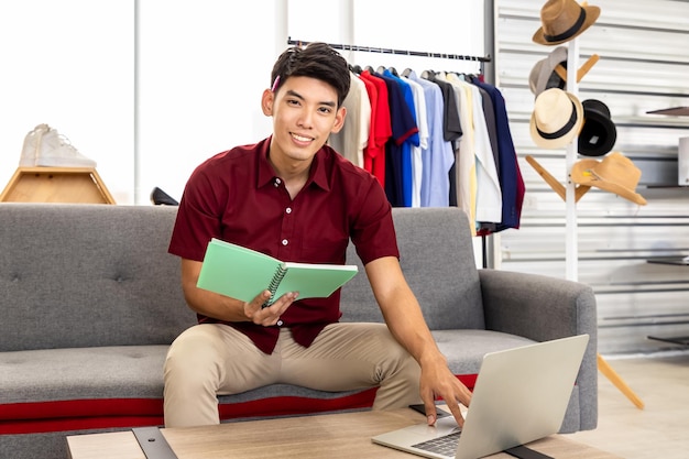 Junger asiatischer männlicher Online-Händler, freiberuflicher Blogger arbeitet zu Hause mit Laptop Social Media Influencer und Online-Shopping-Konzept Blick in die Kamera