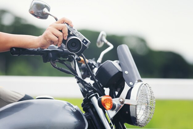 Junger asiatischer männlicher Reisender und Fotograf, die auf dem klassischen Artrennläufermotorrad hält Kamera sitzt