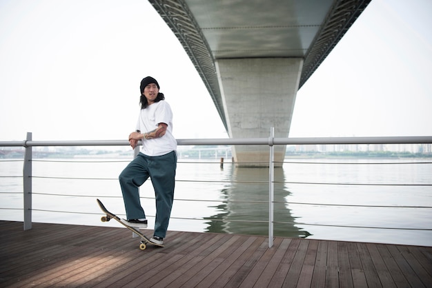 Kostenloses Foto junger asiatischer mann, der draußen in der stadt skateboard fährt