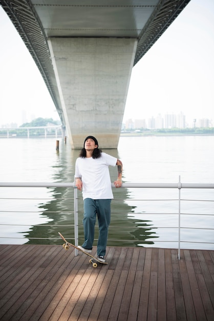 Kostenloses Foto junger asiatischer mann, der draußen in der stadt skateboard fährt