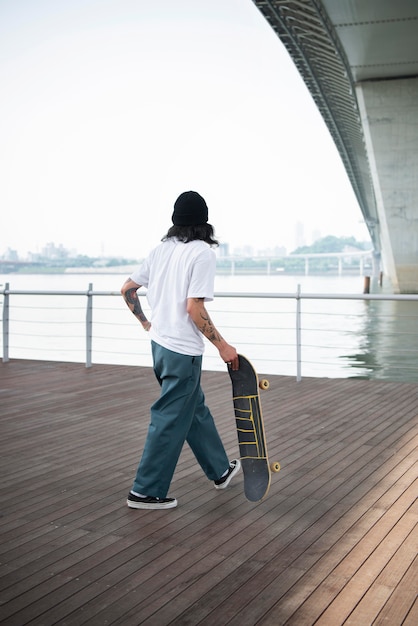 Junger asiatischer Mann, der sein Skateboard hält