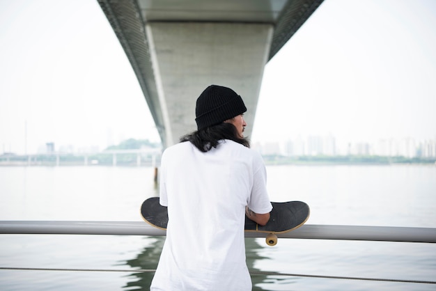 Kostenloses Foto junger asiatischer mann, der sein skateboard hält