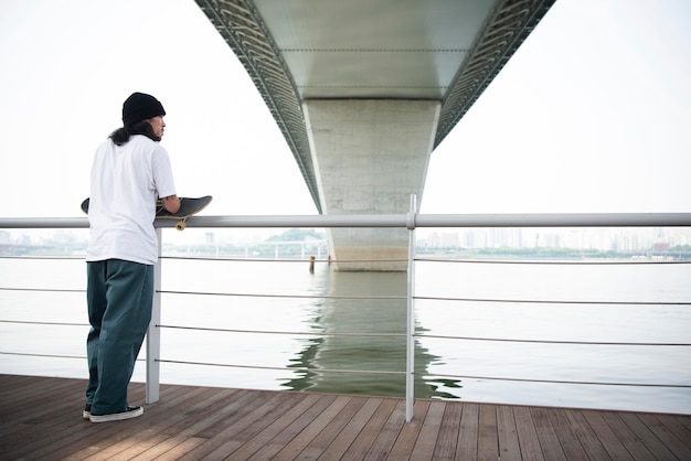 Junger asiatischer Mann, der sein Skateboard hält