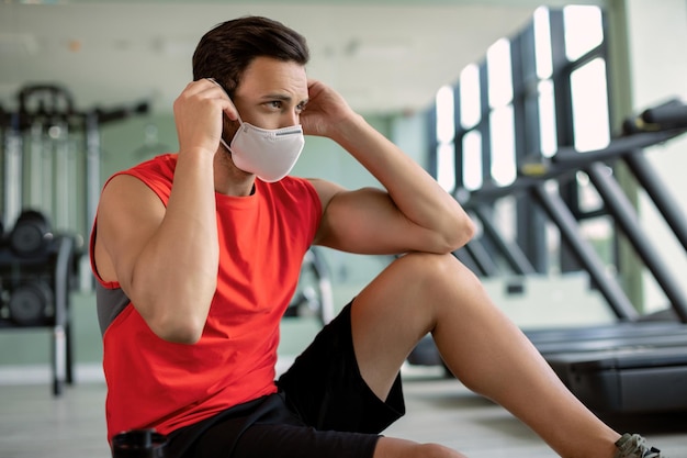 Junger Athlet, der vor dem Sporttraining in einem Fitnessstudio eine schützende Gesichtsmaske aufsetzt