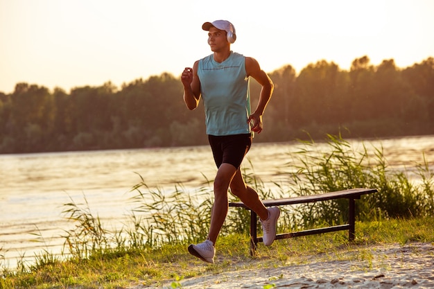 Kostenloses Foto junger athletischer mann beim training, musikhören am flussufer im freien.