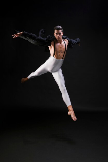 Junger athletischer Mann, der auf schwarzen Hintergrund springt und tanzt