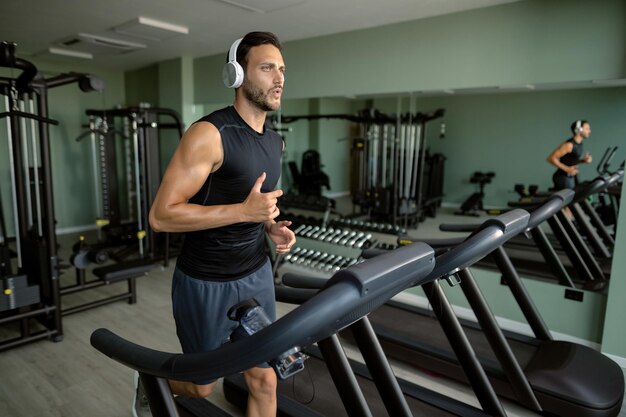 Junger athletischer Mann, der in einem Fitnessstudio auf dem Laufband läuft