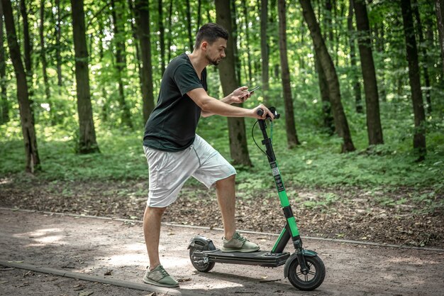 Junger attraktiver Mann, der sein Smartphone benutzt, während er mit Elektroroller auf der Straße steht.