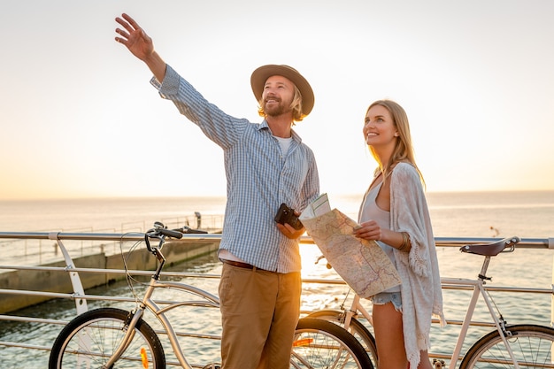 Junger attraktiver Mann und Frau, die auf Fahrrädern reisen, Karte und Besichtigung halten, romantisches Paar in den Sommerferien am Meer am Sonnenuntergang, Freunde, die Spaß zusammen haben