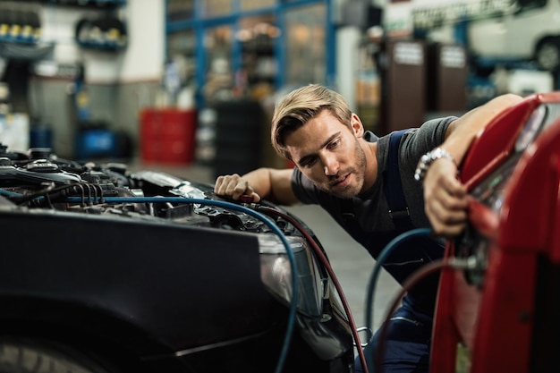 Kostenloses Foto junger automechaniker, der einen kompressor verwendet, während er die klimaanlage eines autos in der werkstatt wartet