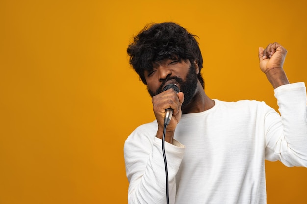 Junger bärtiger Afroamerikaner singt im Mikrofon vor gelbem Hintergrund