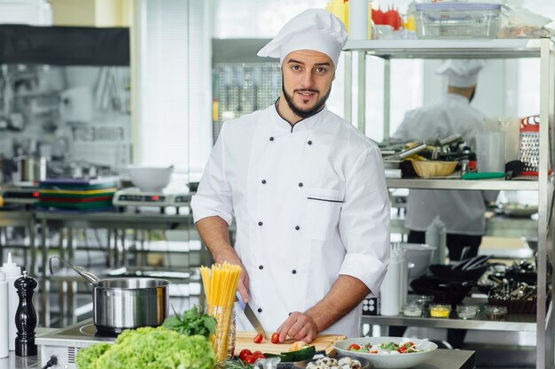 Junger bärtiger Mann an seinem Arbeitsplatz, der Gemüse kocht