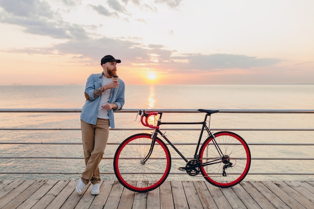 Junger bärtiger Mann, der auf Fahrrad am Sonnenuntergangmeer reist