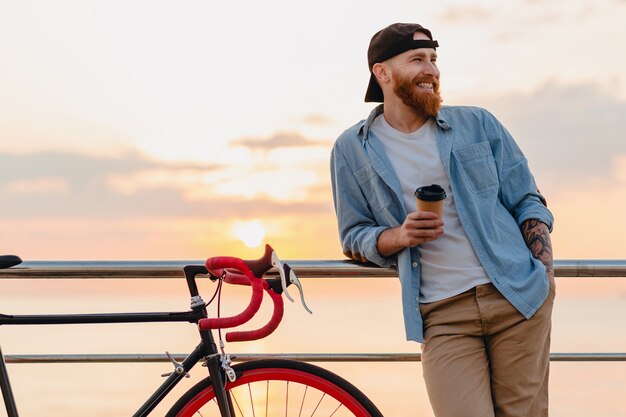 Junger bärtiger Mann, der auf Fahrrad am Sonnenuntergangmeer reist