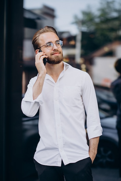 Junger bärtiger Mann, der Telefon benutzt und auf die Straße geht