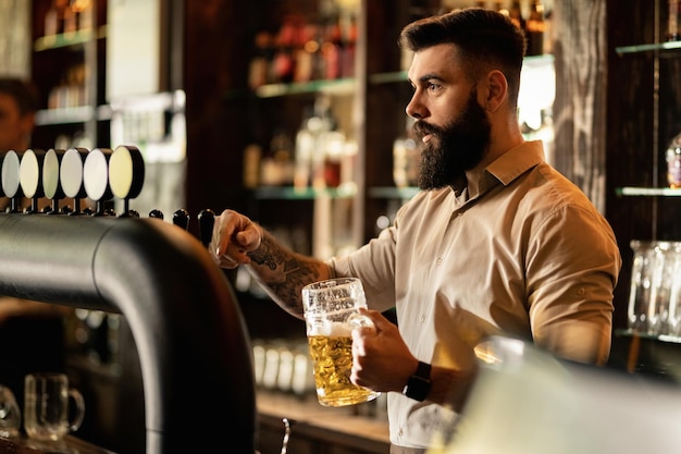 Kostenloses Foto junger barkeeper gießt bier in bierglas, während er an der theke arbeitet.