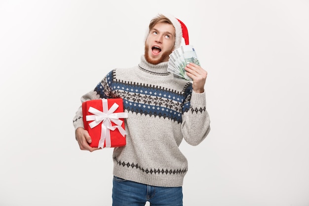 junger Bartmann, der eine Weihnachtsgeschenkbox und Geld auf Weiß hält