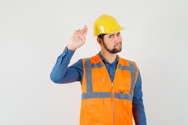 Junger Baumeister, der mit Hand und Fingern im Hemd gestikuliert