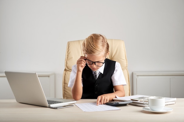 Junger blonder kaukasischer junge, der am exekutivschreibtisch im büro sitzt und dokumente studiert