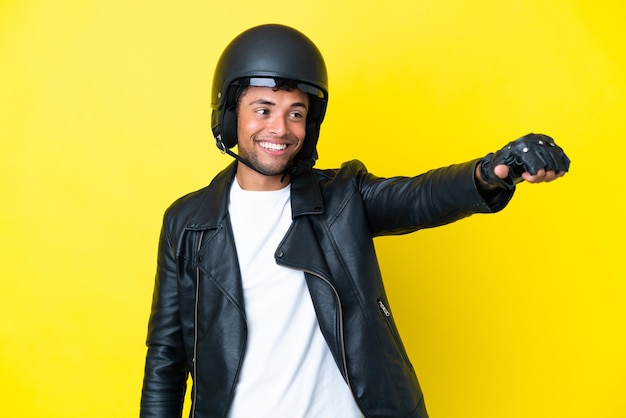 Junger brasilianischer mann mit einem motorradhelm auf gelbem hintergrund isoliert, der eine geste mit dem daumen nach oben gibt