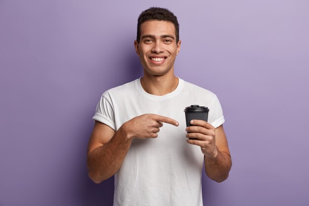 Junger Brunetmann, der weißes T-Shirt trägt, das auf Tasse Kaffee zeigt